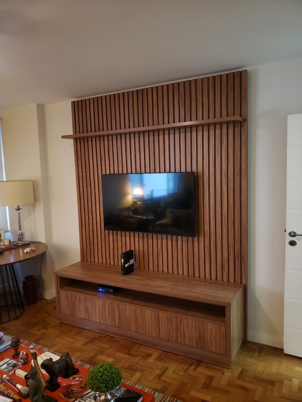 painel de tv ripado amadeirado com uma tv ao centro e um home na parte de baixo